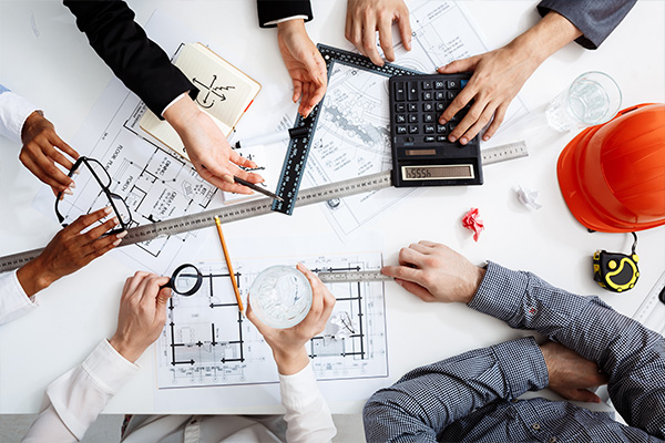 Top-down view of a design team collaborating on blueprints with rulers, a calculator, and a hard hat, demonstrating architecture services in India.